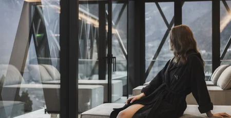 Le migliori referenze per il nostro marketing alberghiero Donna in accappatoio seduta su divano guarda il paesaggio montano attraverso grandi finestre