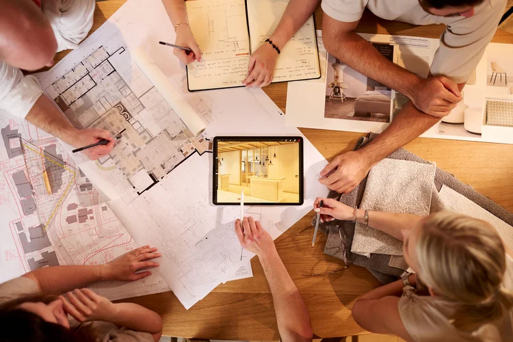 Wie entsteht ein außergewöhnliches Hotel? Team bespricht Grundrisse und Materialmuster; ein Tablet zeigt einen hellen Innenraum