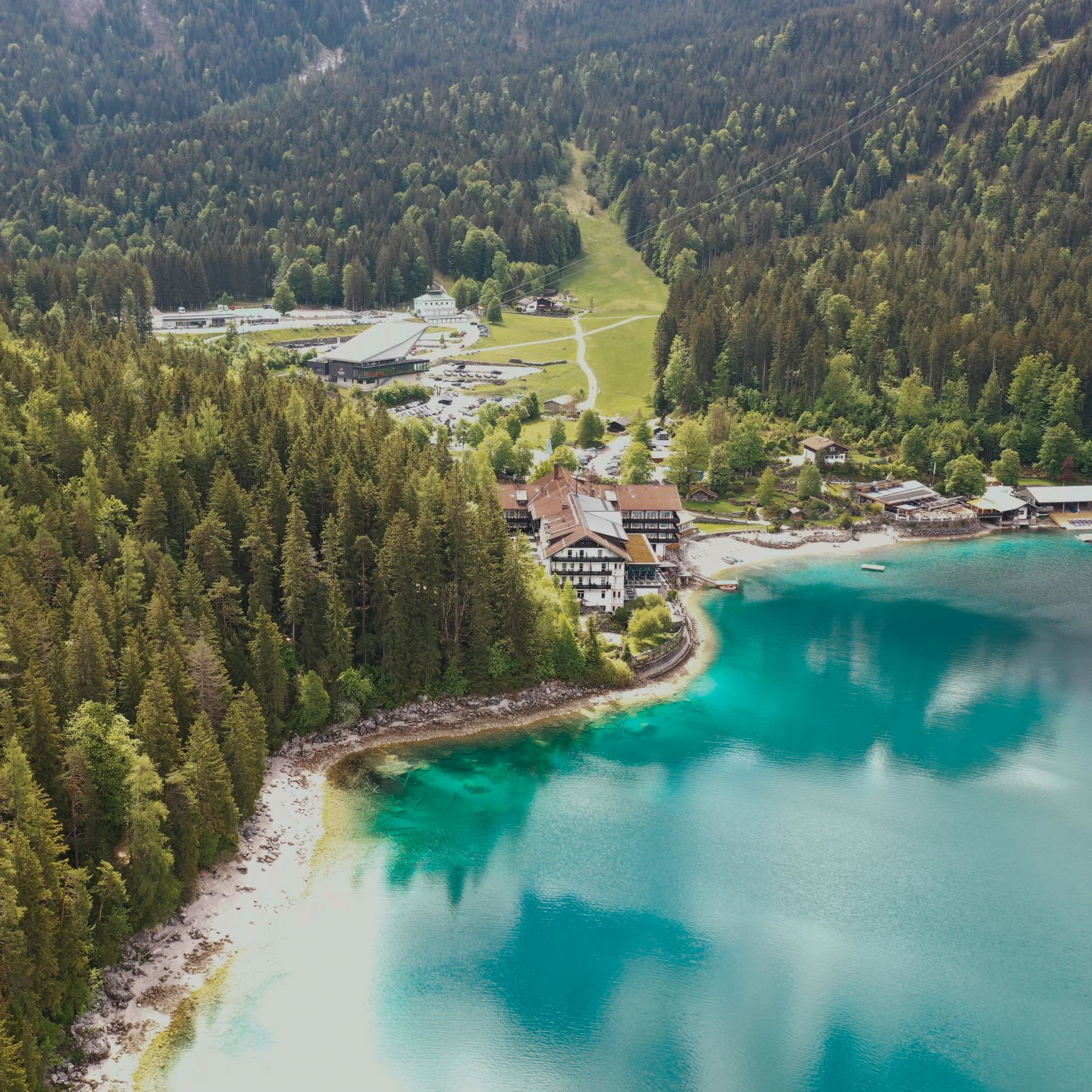 Aerial view of a hotel by turquoise lake surrounded by forest and mountains