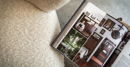 Aufgeschlagenes Buch mit Bildern eines Mannes und Inneneinrichtungen auf einem Sofa