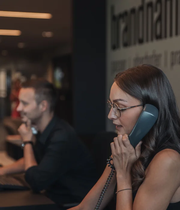 Woman talking on phone in modern office with man working on computer behind