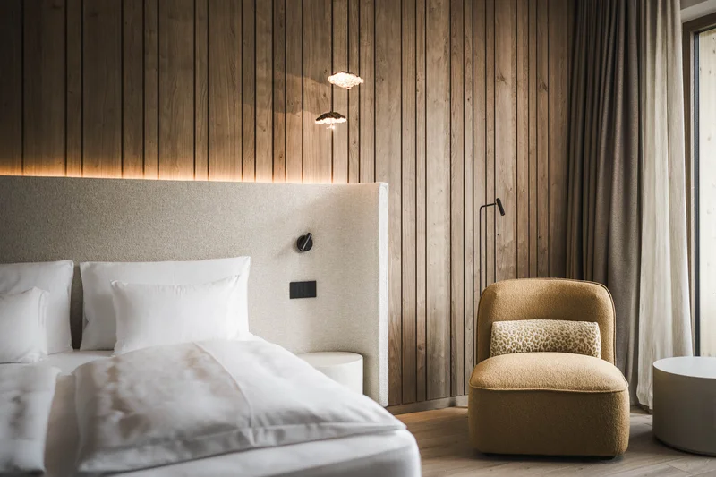 Follow the call of the mountains to St. Vigil Modern bedroom with wood wall, cozy armchair, and bed with white bedding