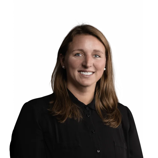 Frau mit braunen Haaren und schwarzem Hemd lächelt vor weißem Hintergrund