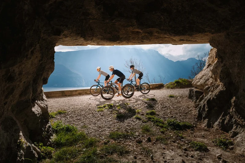 AktivHotel SantaLucia: Vom Tool-Chaos zur digitalen Einheit am Gardasee Drei Radfahrer mit Helmen fahren entlang eines Bergwegs, gesehen von einer Höhle aus