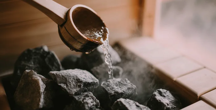Wasser wird mit einer Holzschöpfkelle auf heiße Steine in der Sauna gegossen