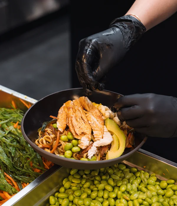 Person wearing black gloves preparing healthy plate with grilled chicken and vegetables