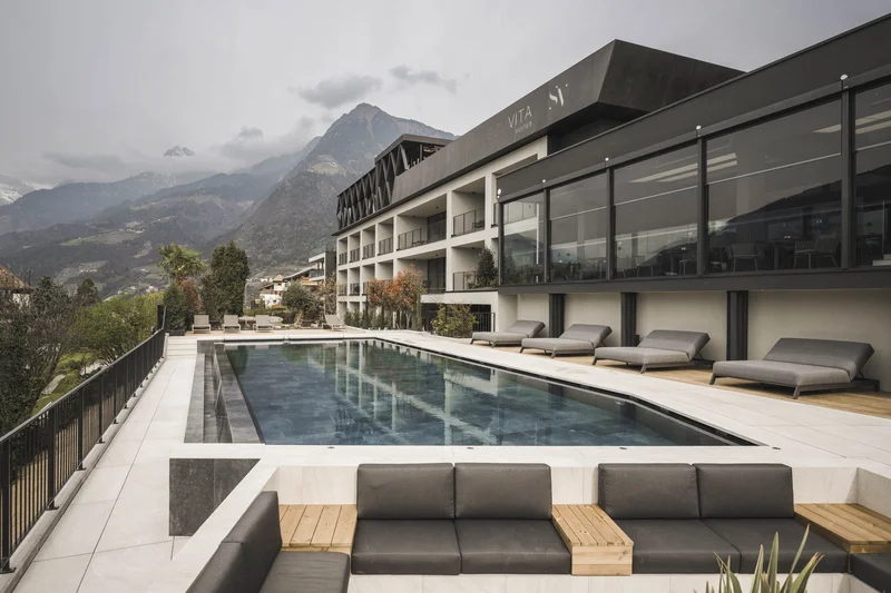 Marketing a 360° per un’esperienza a 360° Piscina moderna in hotel con lettini e vista sulle montagne sotto un cielo nuvoloso