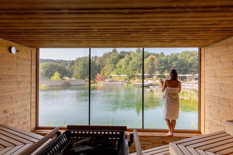 Pfalzblick Wald Spa Resort: posizionamento forte, su internet e fuori Donna in sauna guarda lago e foresta attraverso grande finestra