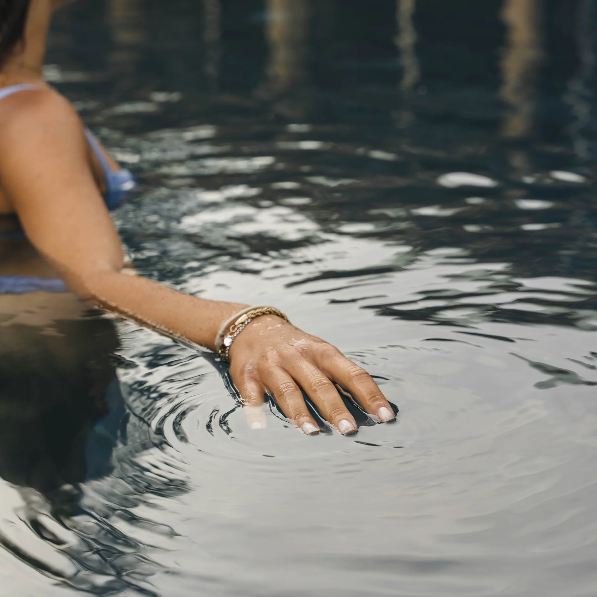 Frau berührt Wasseroberfläche in einem Pool mit sanften Wellen