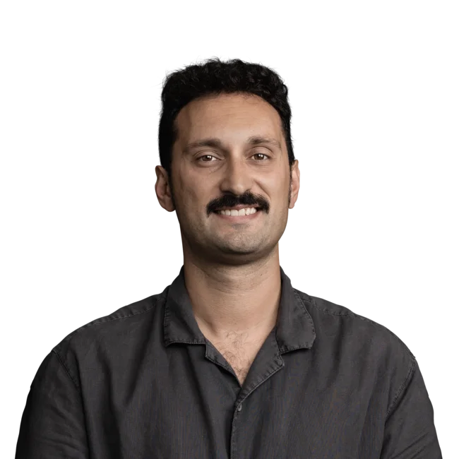 Porträt eines lächelnden Mannes mit dunklem Hemd und Schnurrbart vor weißem Hintergrund