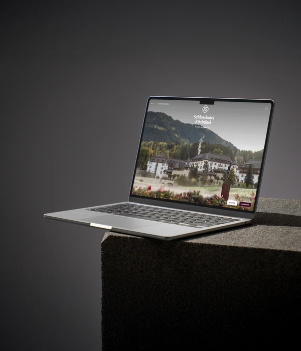 Laptop mit Website des Schlosshotels Kitzbühel vor grau-schwarzem Hintergrund