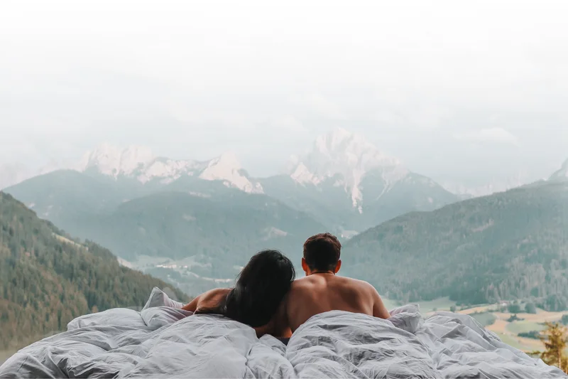 A stylish new website for the Alpen Tesitin in South Tyrol Couple in bed looking at forested mountains and valleys