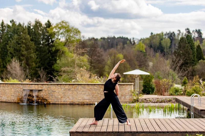 Pfalzblick Wald Spa Resort: posizionamento forte, su internet e fuori Donna fa yoga su una passerella di legno sul lago con bosco sullo sfondo