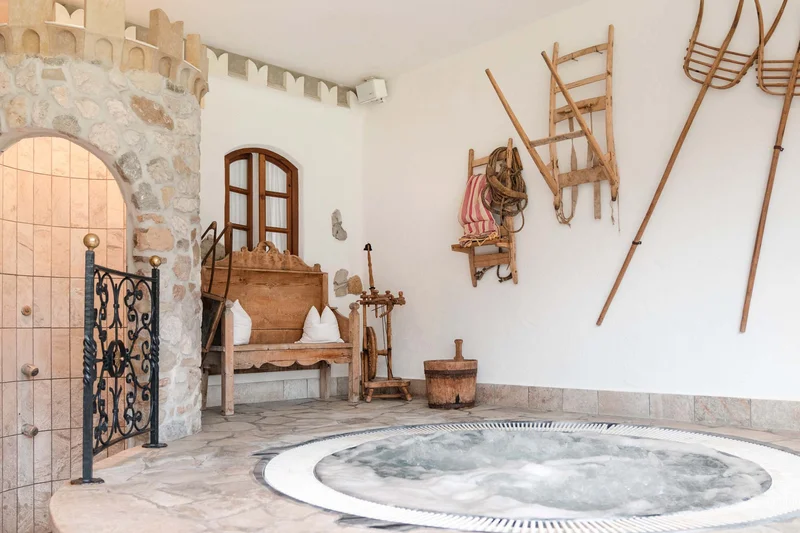 Wellness area with hot tub, rustic wooden bench, and traditional tools on the wall
