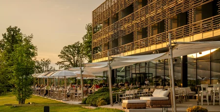 Die besten Referenzen für unser Hotelmarketing Außenrestaurant mit Sitzplätzen und Sonnenschirmen neben modernem Gebäude bei Sonnenuntergang