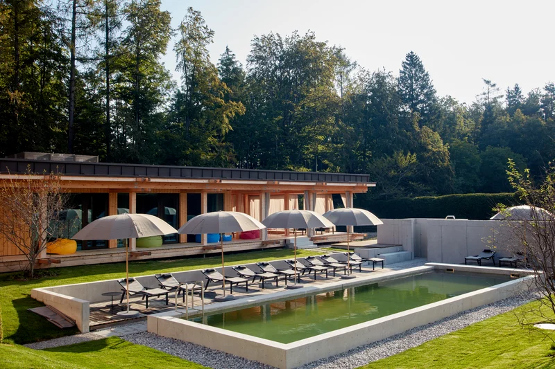 Moderner Außenpool mit Liegestühlen und Sonnenschirmen vor Holzhaus im Wald