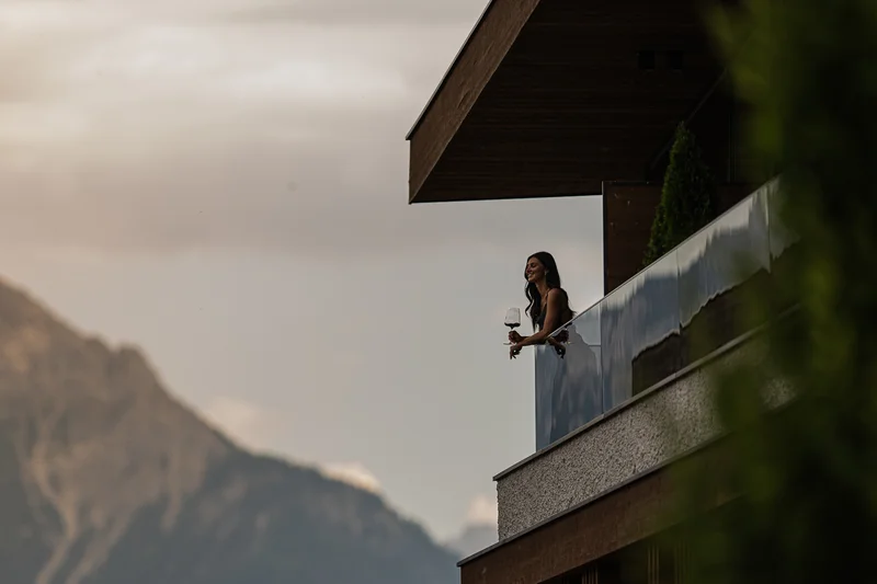 A stylish new website for the Alpen Tesitin in South Tyrol Woman with wine glass on balcony overlooking mountain under cloudy sky