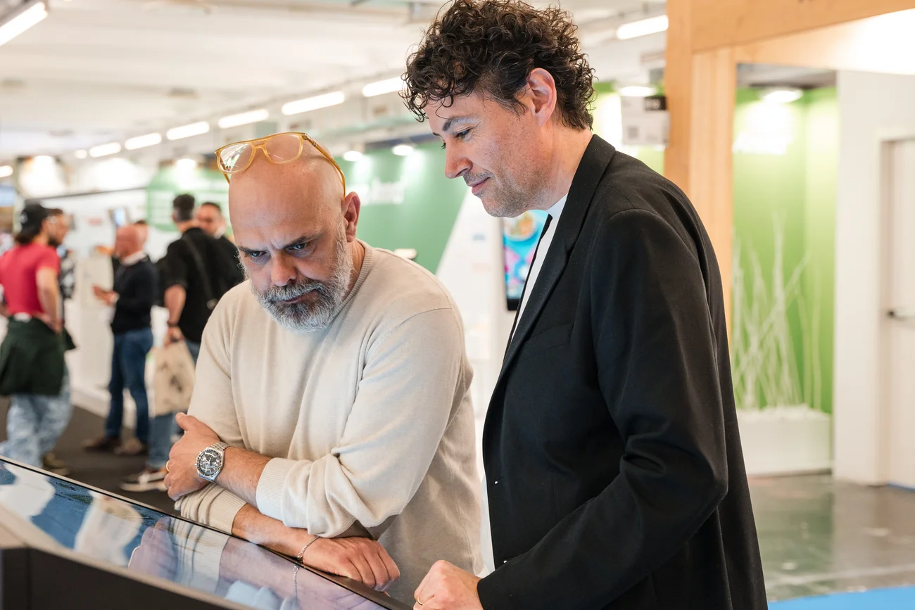Zwei Männer arbeiten gemeinsam an einem interaktiven Touchscreen in einer Ausstellung