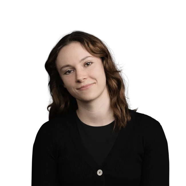 Sarah Indra Giovane donna con capelli castani ricci, sorriso gentile, maglia nera