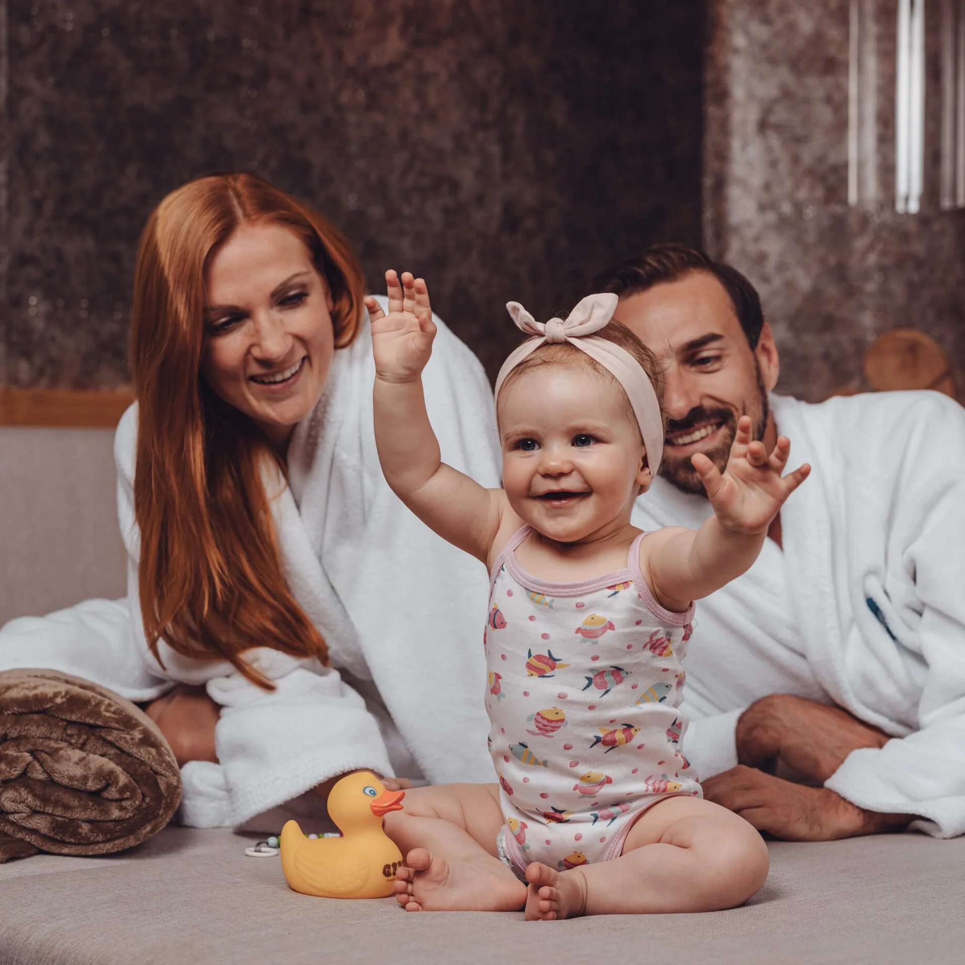 Die Familienhotels Südtirol – branded by Brandnamic Glückliche Familie mit Baby und Quietscheente auf Sofa zu Hause