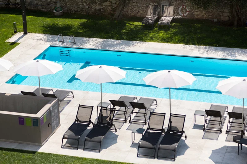 AktivHotel SantaLucia: Vom Tool-Chaos zur digitalen Einheit am Gardasee Moderner Außenpool mit Liegestühlen und weißen Sonnenschirmen neben Rasen