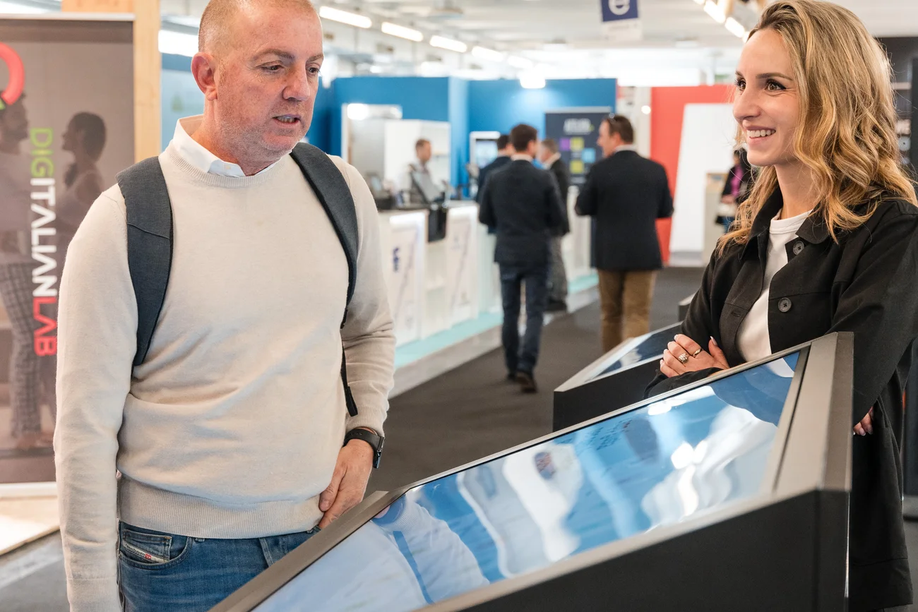 Mann und Frau schauen auf einen großen Touchscreen bei einer Ausstellung