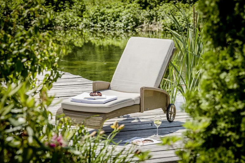 Liegestuhl mit Kissen am Teich mit Handtuch und Sonnenbrille