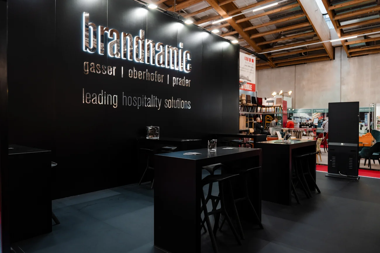Messeausstellung mit Brandnamic-Hospitality-Lösungen und schwarzen Möbeln