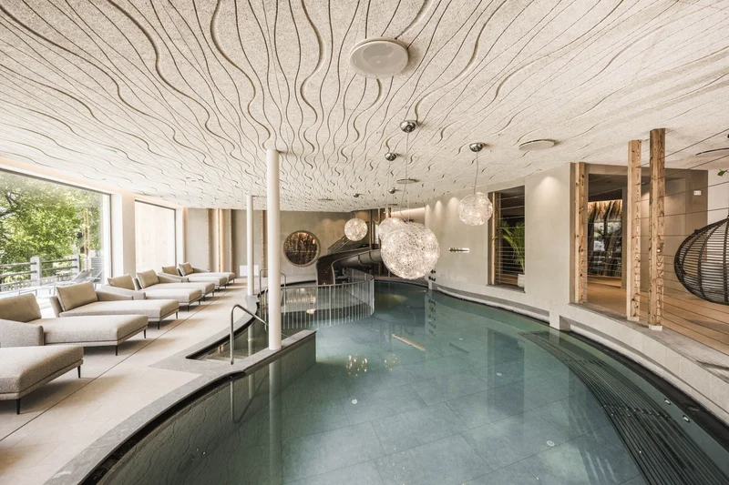 Follow the call of the mountains to St. Vigil Modern indoor pool with lounge chairs and wavy ceiling design