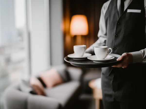 Kellner trägt zwei Tassen Kaffee auf Tablett in gemütlichem Hotelzimmer