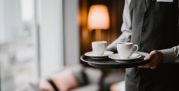 Kellner trägt zwei Tassen Kaffee auf Tablett in gemütlichem Hotelzimmer
