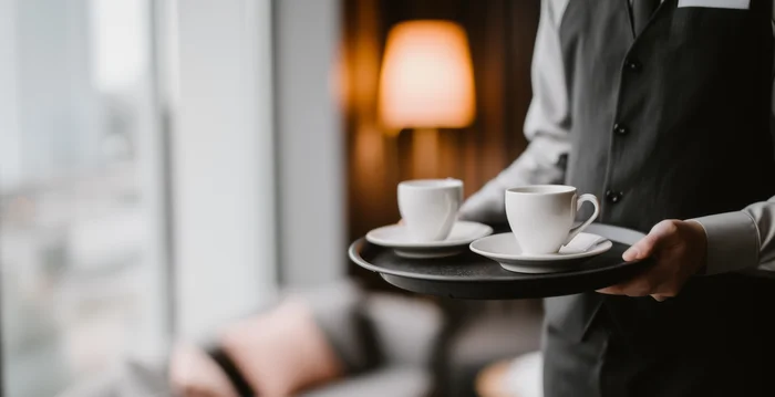 Cameriere che porta due tazze di caffè su un vassoio in una stanza d'hotel accogliente