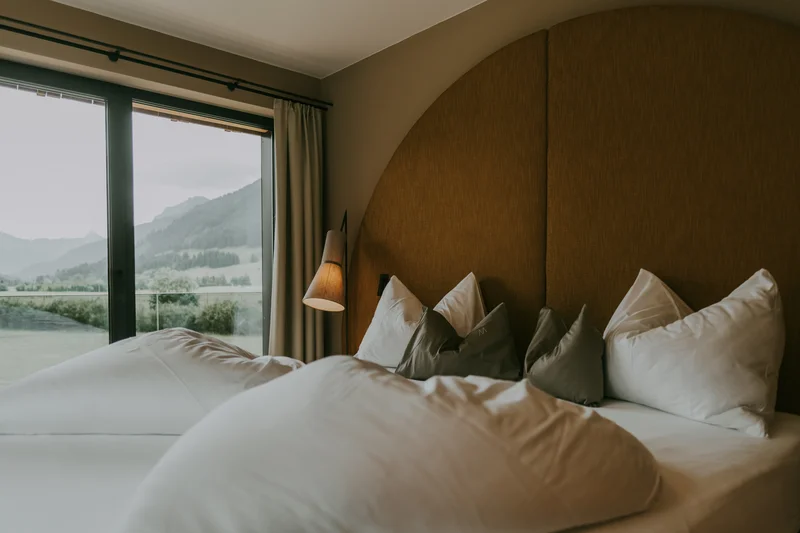Gemütliches Bett mit vielen Kissen und Bergblick durch Fenster