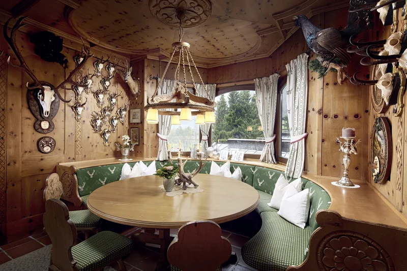 Rustikaler Essbereich mit Holztisch, grünen Sitzpolstern und Trophäen an den Wänden