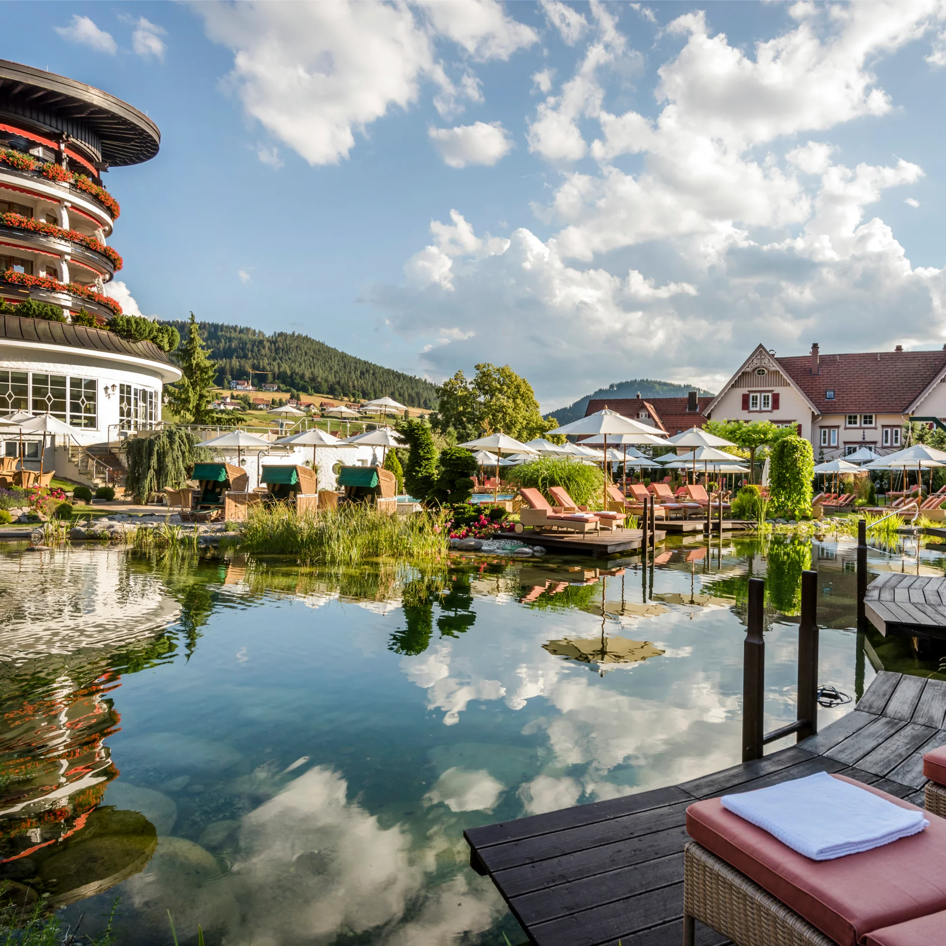 Hotel mit Teich, Liegestühlen und Sonnenschirmen bei sonnigem Wetter