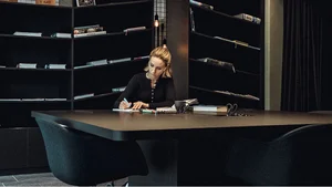 Frau schreibt Notizen an einem großen Tisch in einem modernen Raum mit Bücherregalen