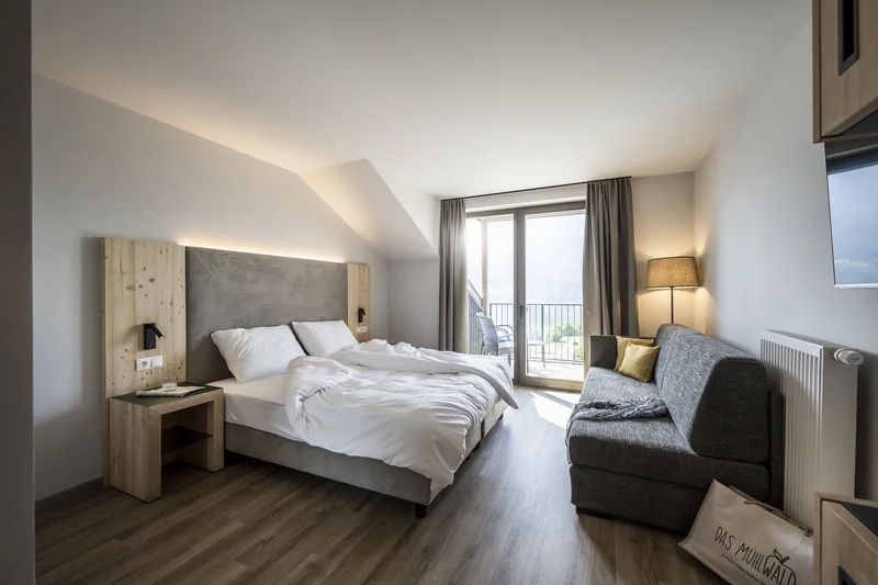 Das Mühlwald: Strategic realignment and sales setup lead to a 50% increase in turnover Modern hotel room with bed, sofa, and balcony overlooking mountain view
