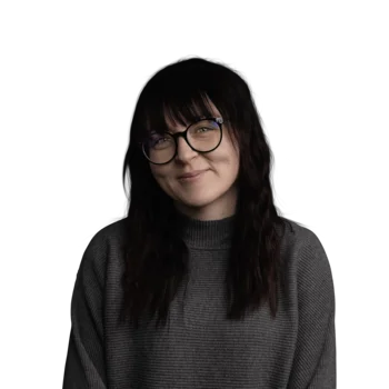 Frau mit langen dunklen Haaren, Brille und grauem Pullover lächelt freundlich