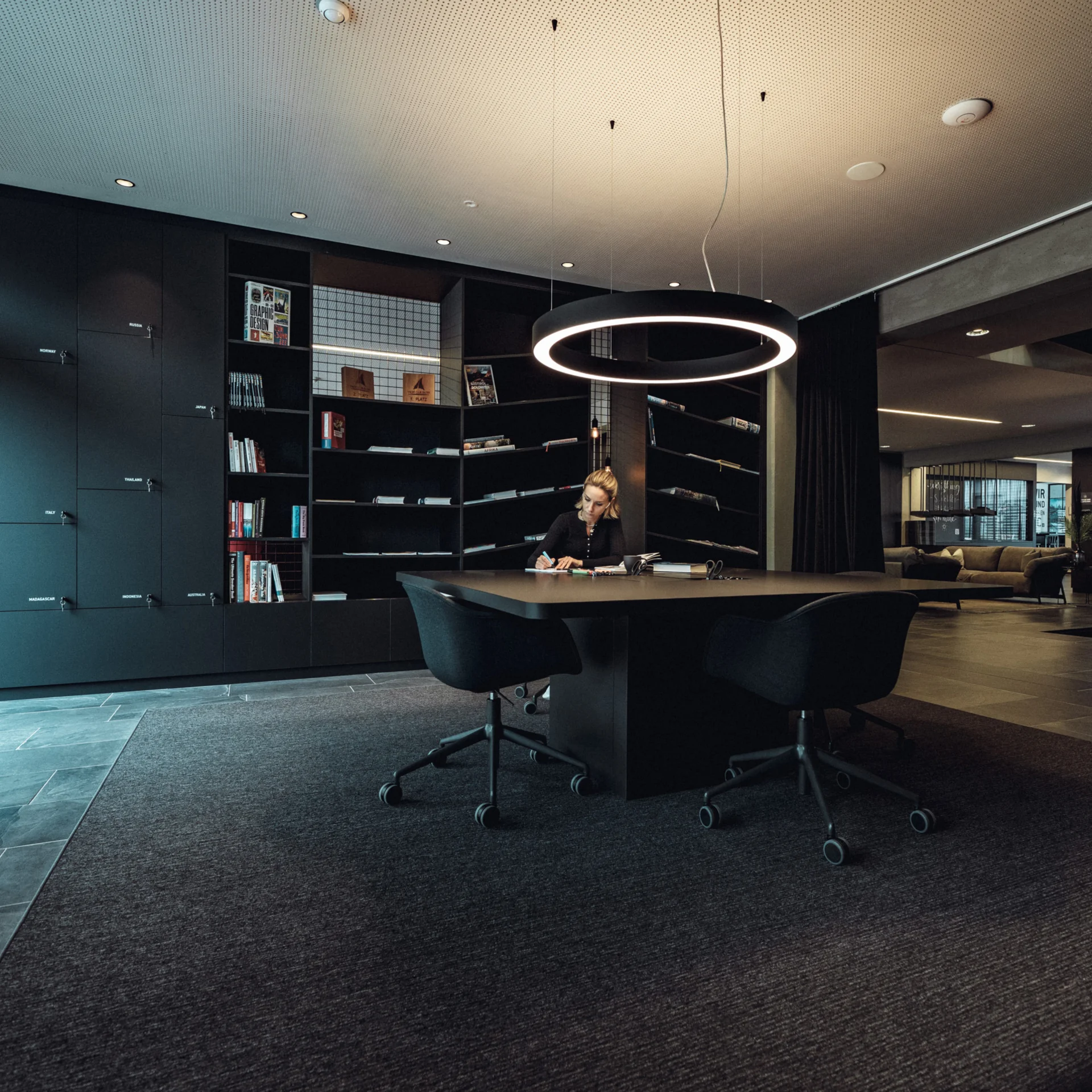 Frau sitzt an einem Tisch in modernem Büro mit Bücherregalen und Beleuchtung