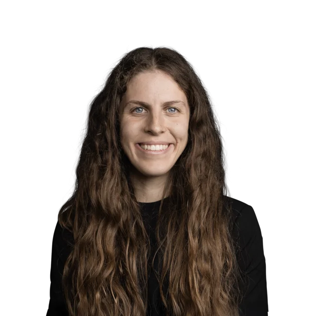 Porträt einer lächelnden Frau mit langen, lockigen Haaren und schwarzem Oberteil