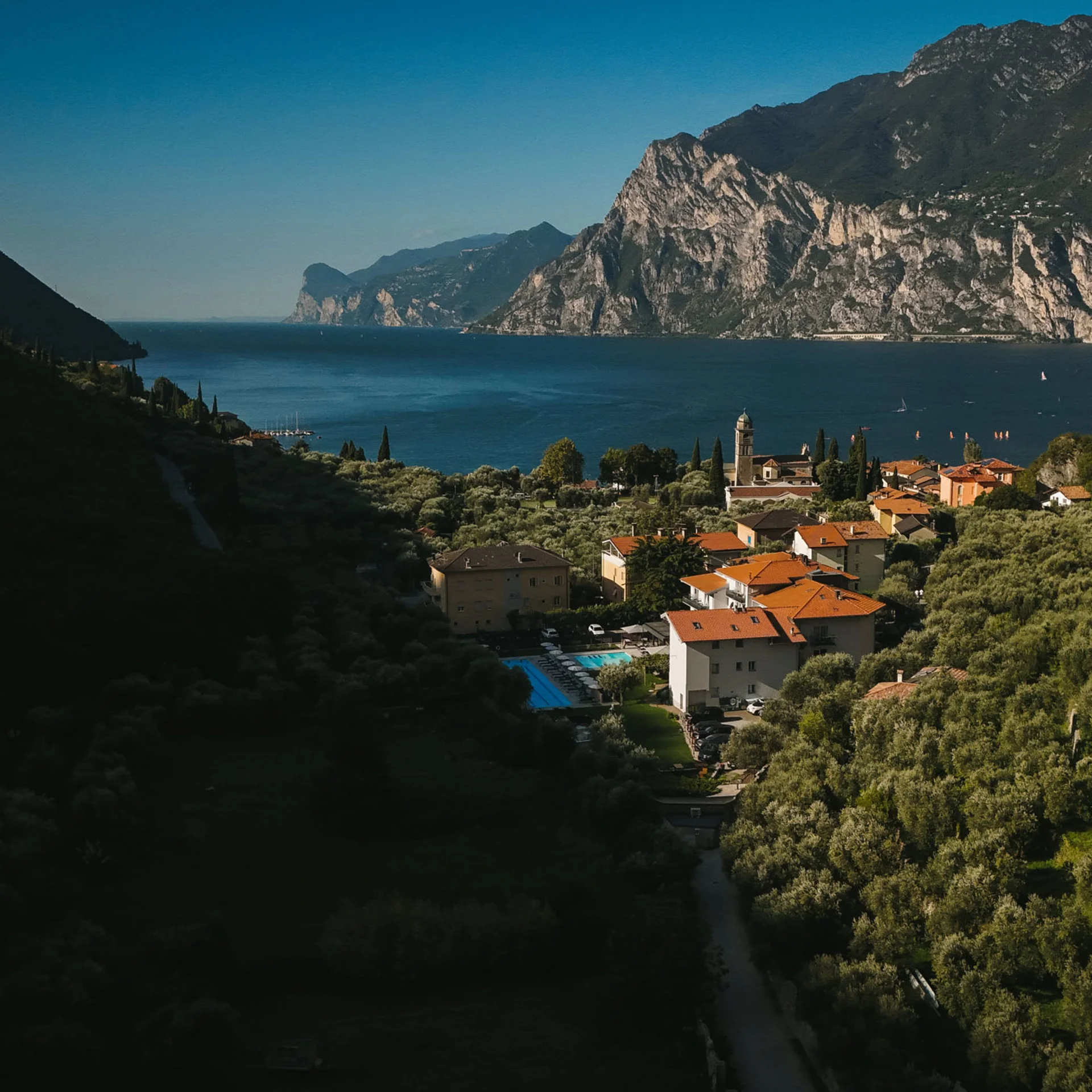 AktivHotel SantaLucia: Vom Tool-Chaos zur digitalen Einheit am Gardasee Dorf am Seeufer umgeben von Bergen und grünen Wäldern bei klarem Himmel