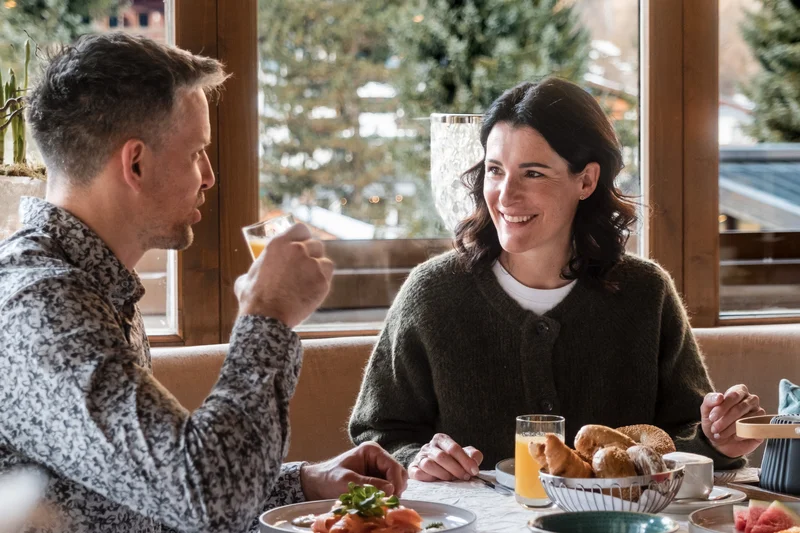 Paar beim Frühstück mit Blick auf verschneite Tannenbäume draußen