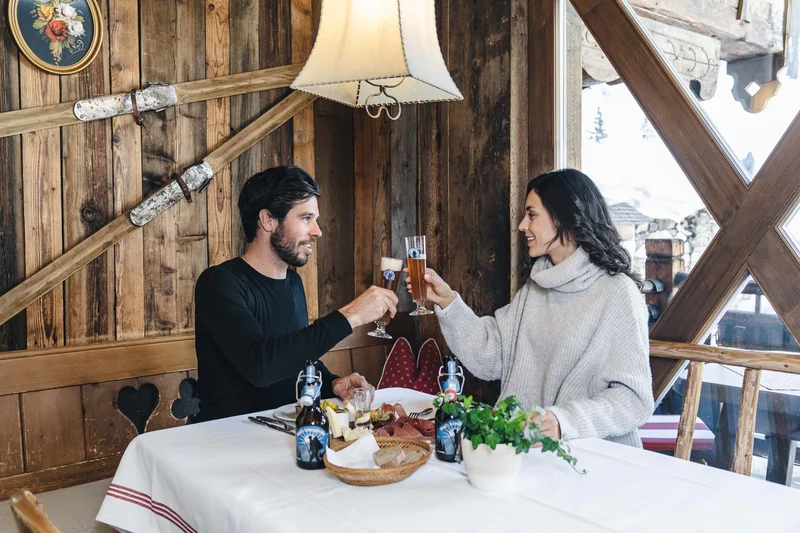 Paar stößt mit Biergläsern in gemütlicher Holzhütte an