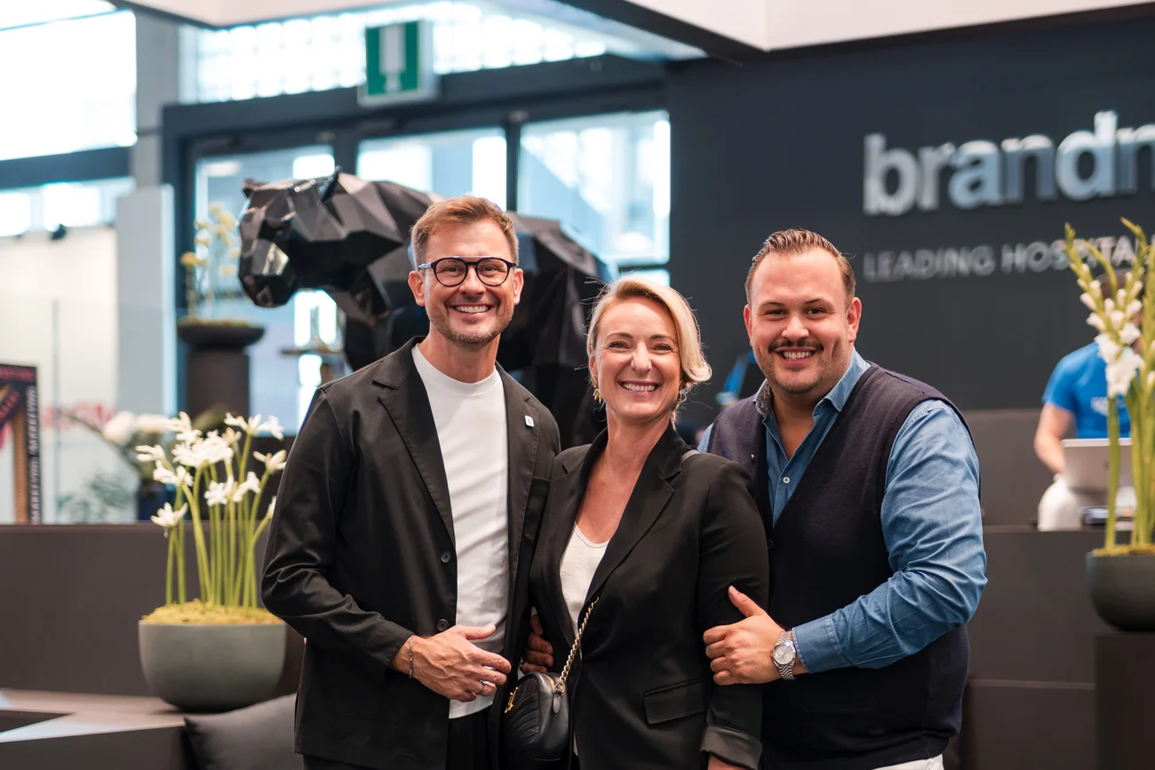 Drei lächelnde Menschen in professioneller Kleidung in modernem Innenraum