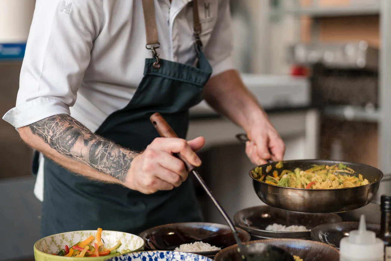 Koch mit Tattoo serviert Gemüse aus der Pfanne in Schüsseln in der Küche