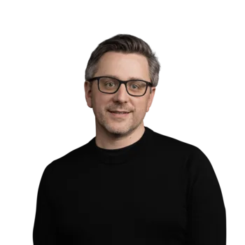 Roland Konzett | Sales Consultant Porträt eines Mannes mit Brille in schwarzem Pullover vor weißem Hintergrund