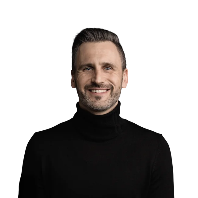 Lächelnder Mann mit schwarzen Pullover und kurzem Haar vor weißem Hintergrund