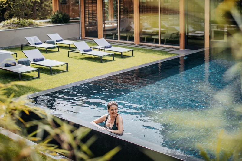 Frau im Pool mit Liegestühlen und Holzhaus im Hintergrund