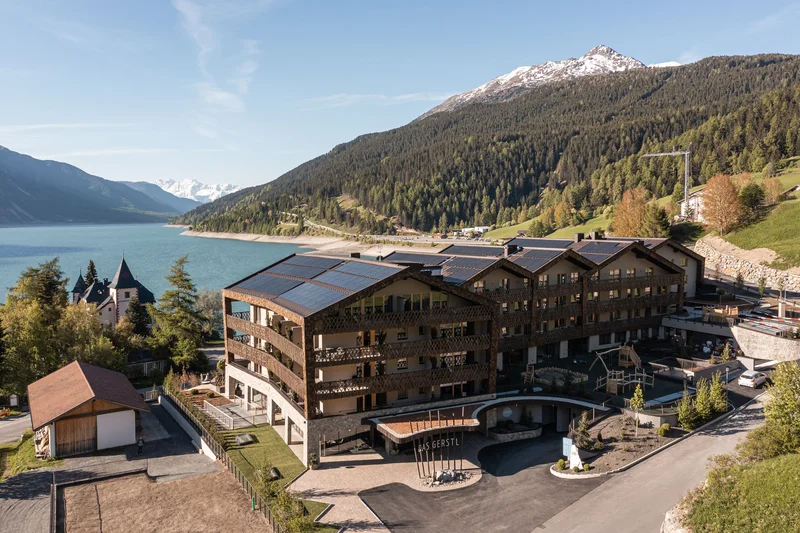 Hotel with solar panels by a lake and forested mountains with snow-capped peak