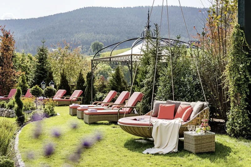 Garten mit Liegestühlen, Hängesessel und Bergblick an sonnigem Tag